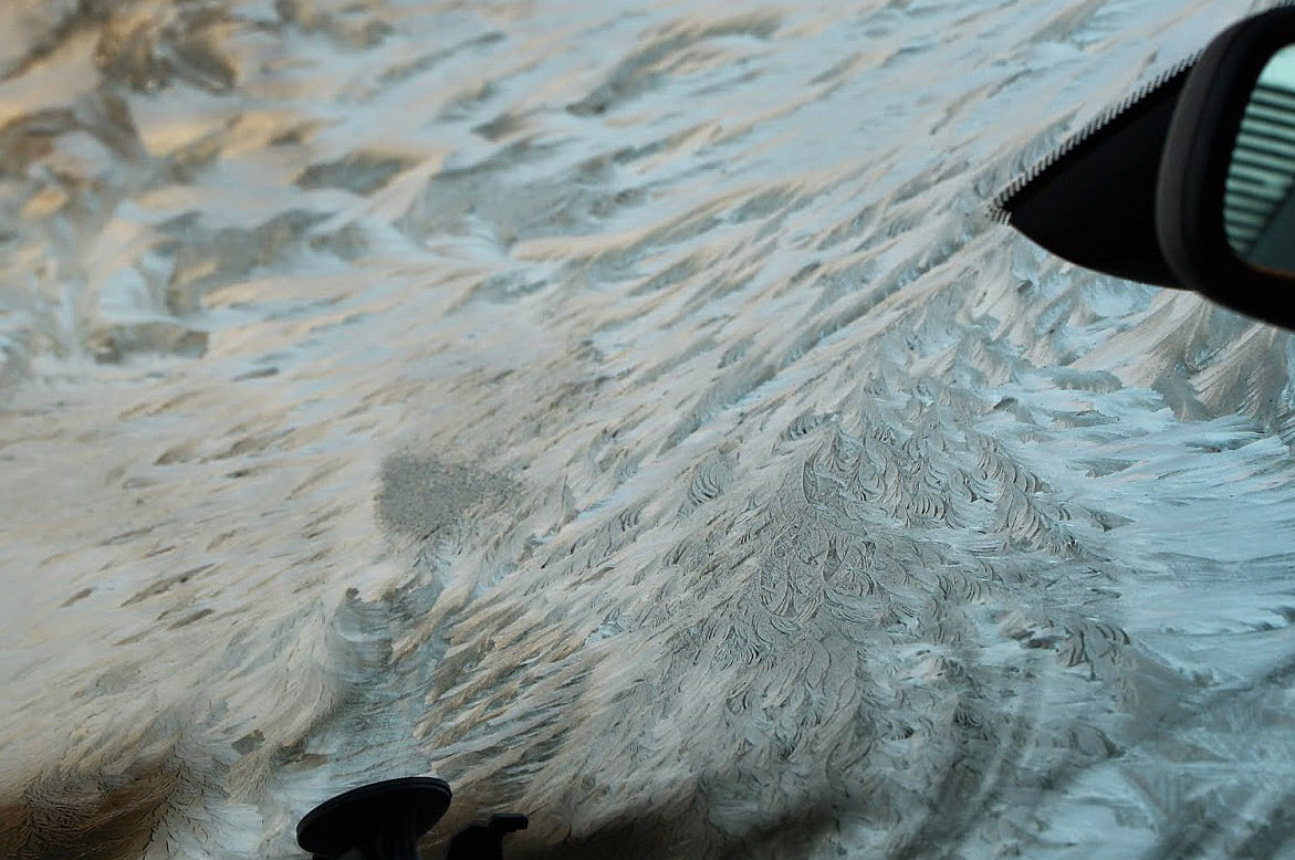 Feathery frost and ice patterns covering a car windshield, viewed from inside