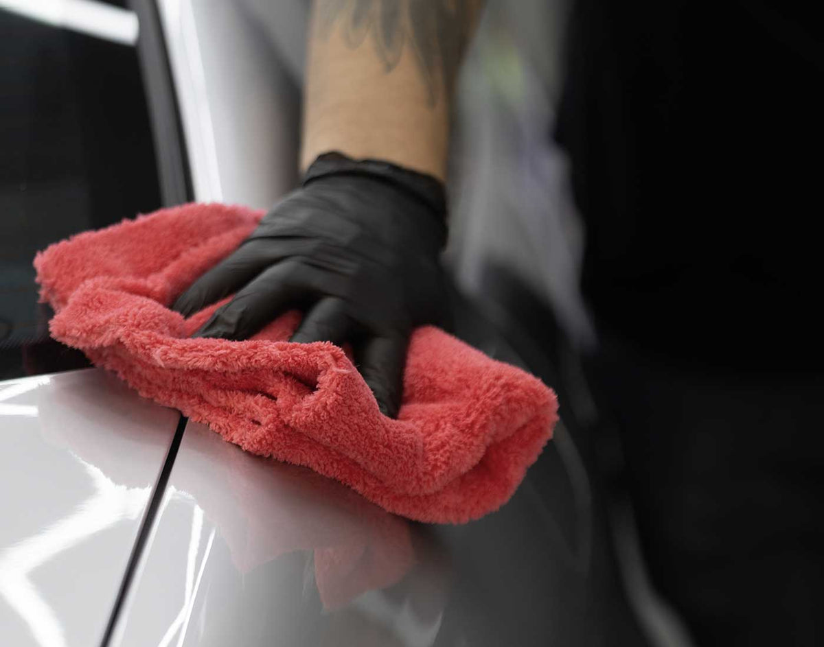 Black-gloved hand wiping a silver vehicle panel with a red microfiber towel