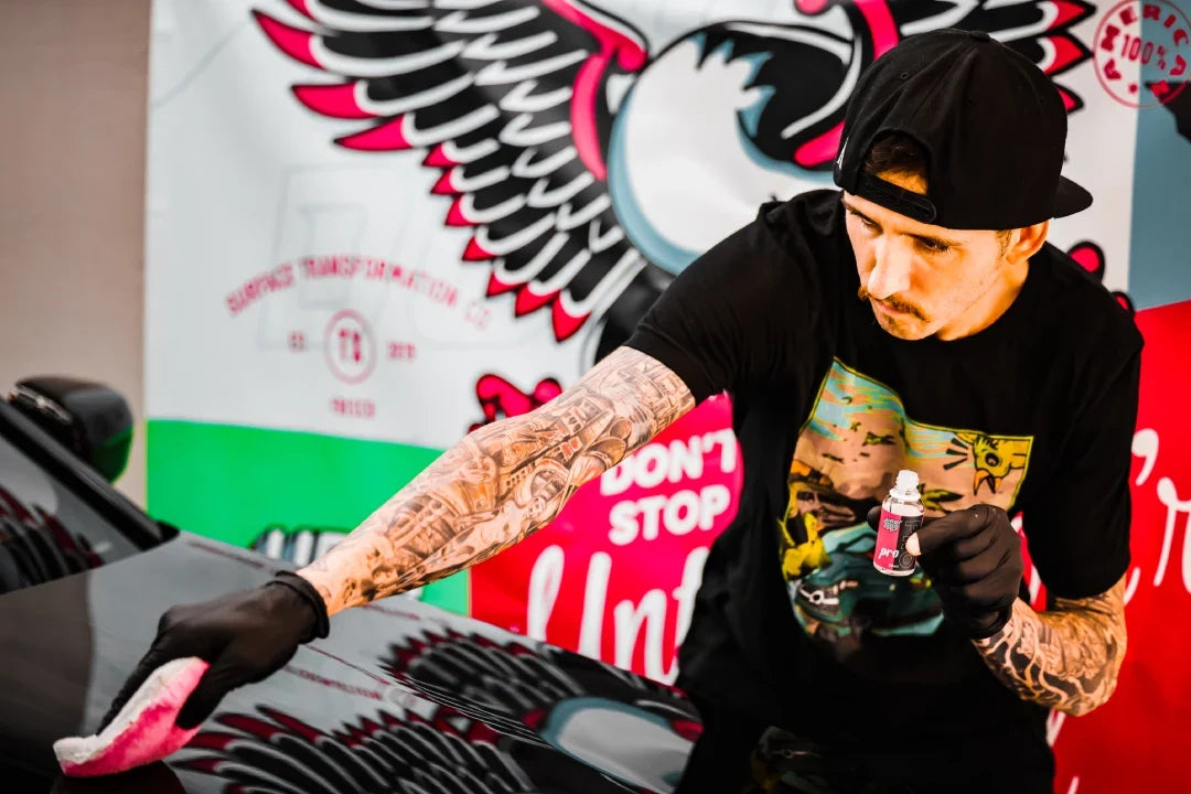 Gloved presenter holding an Undrdog Pro bottle while wiping a black vehicle with a pink cloth