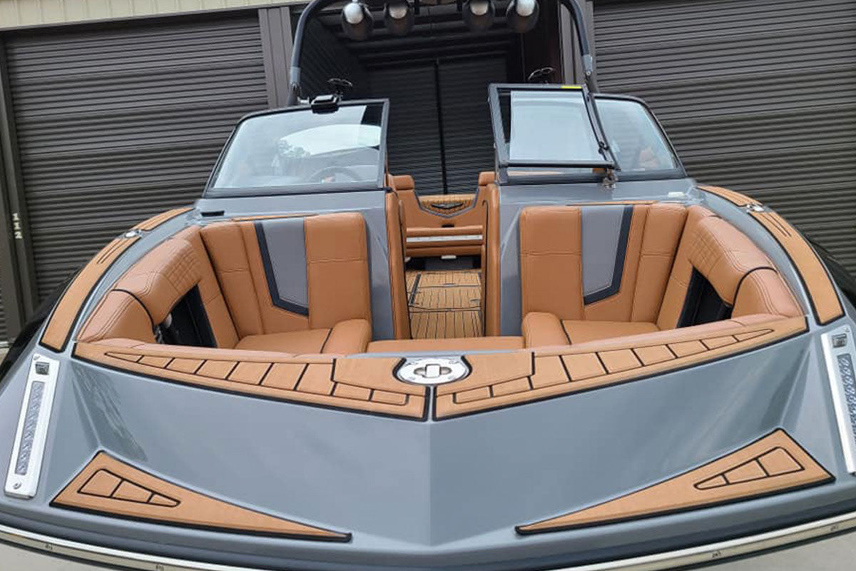 A modern boat with tan cushioned seating, gray and tan paneling, and an open windshield, parked in front of closed dark garage doors.