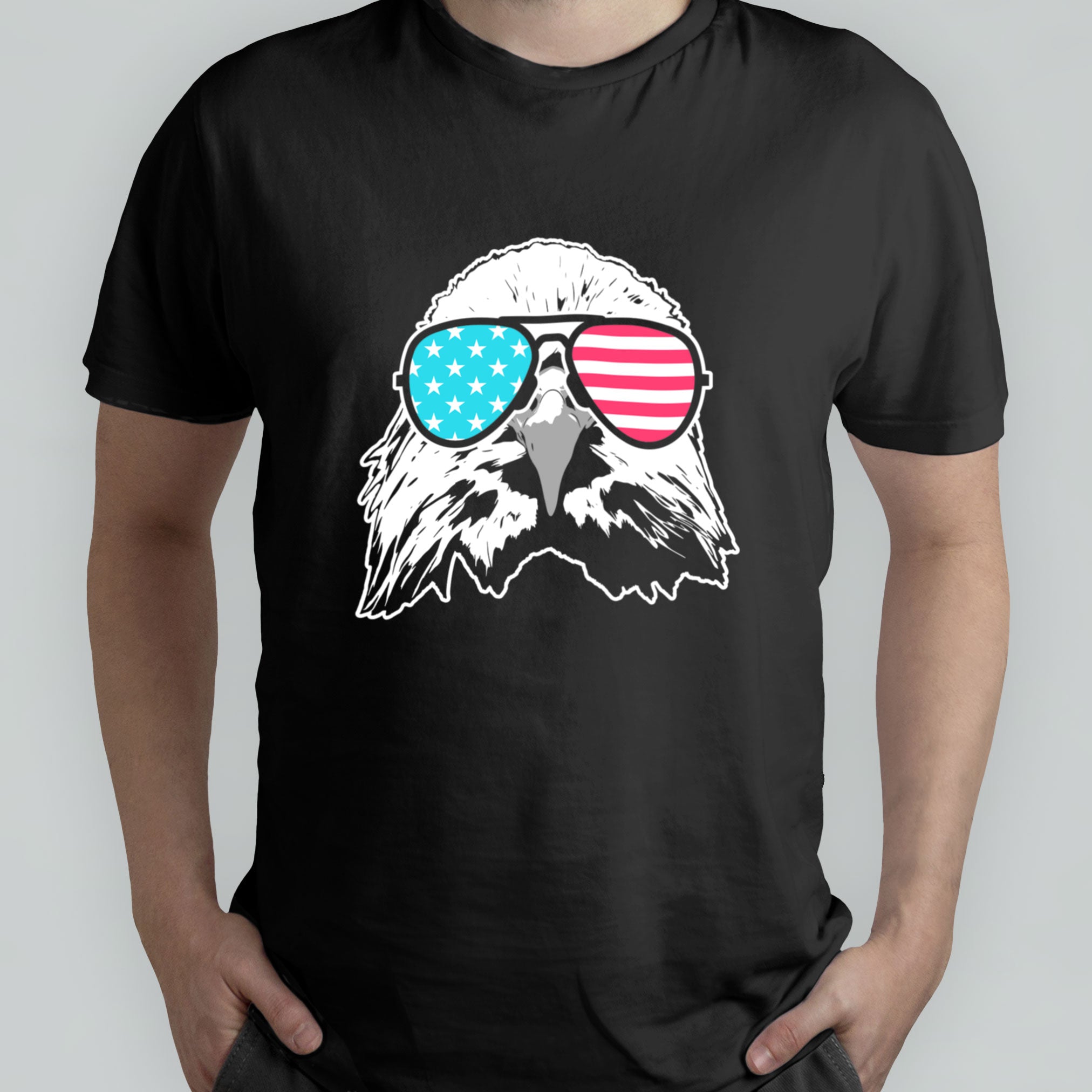 A person wearing a black T-shirt featuring an illustration of a bald eagle head with sunglasses displaying the American flag design on the lenses.