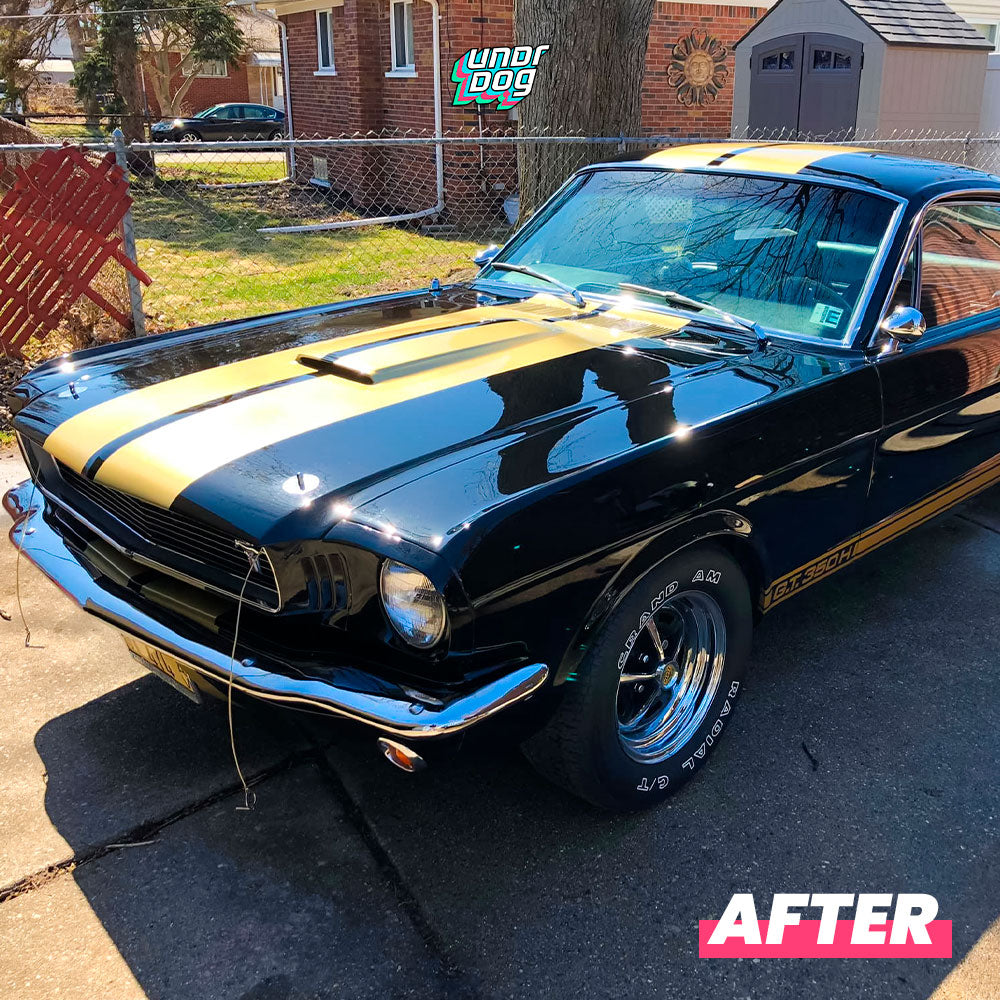 A restored classic black car with yellow racing stripes is parked on a driveway. The car has shiny chrome details and polished wheels. In the background, there is a red fence, a tree, and a shed. Text on the image reads "After.