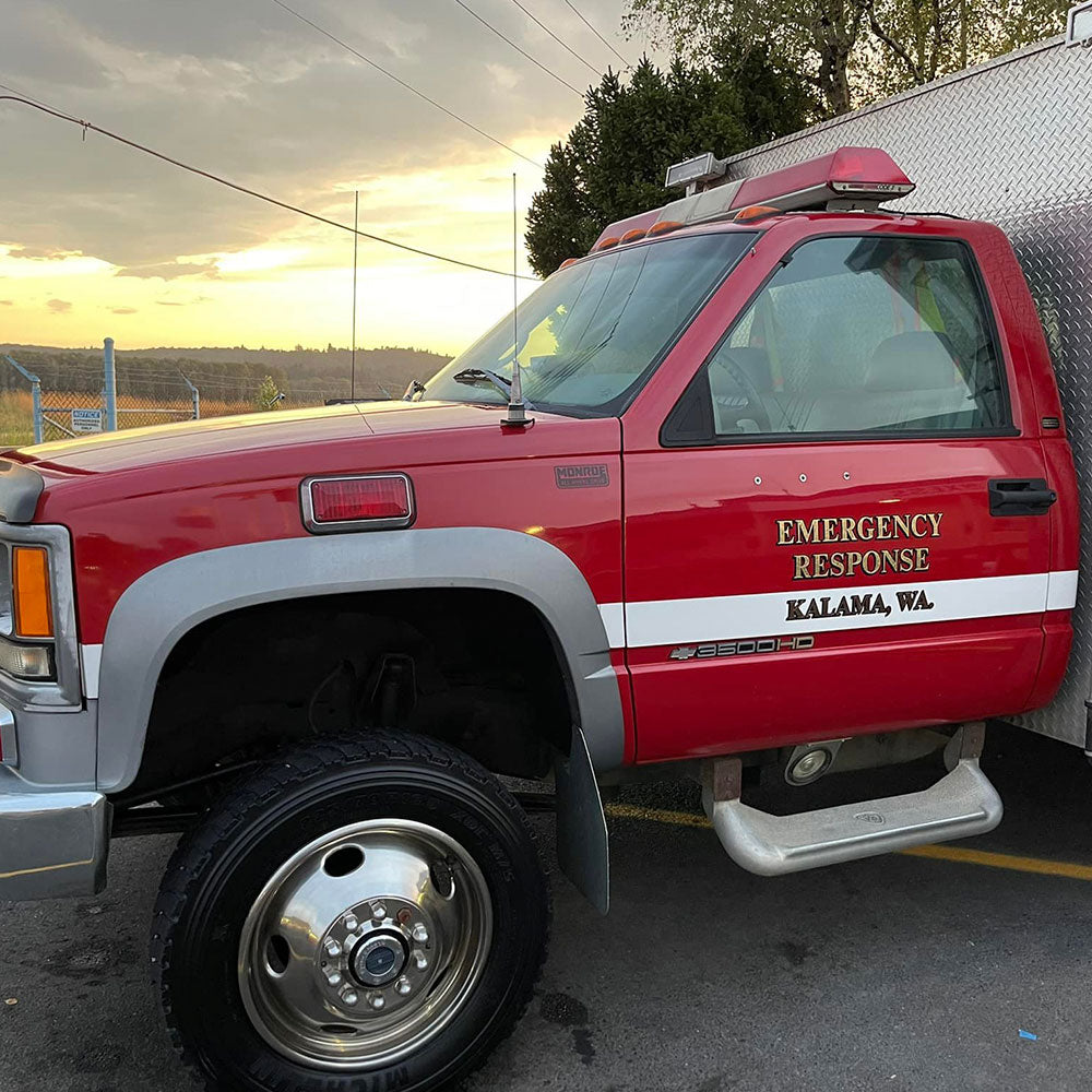 A red emergency response vehicle is parked on a paved surface. The truck features white lettering indicating "Emergency Response Kalama, WA." The setting sun and cloudy sky are visible in the background.