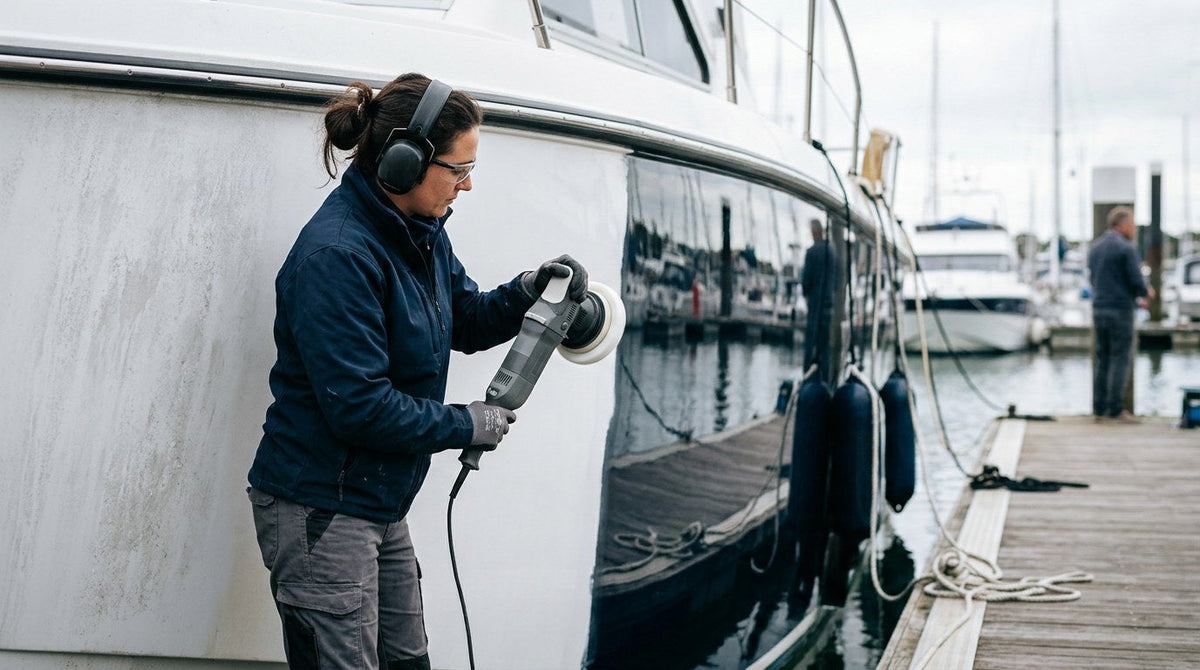 Person polishing fiberglass boat hull with dual-action polisher showing oxidized gel coat transitioning to mirror gloss
