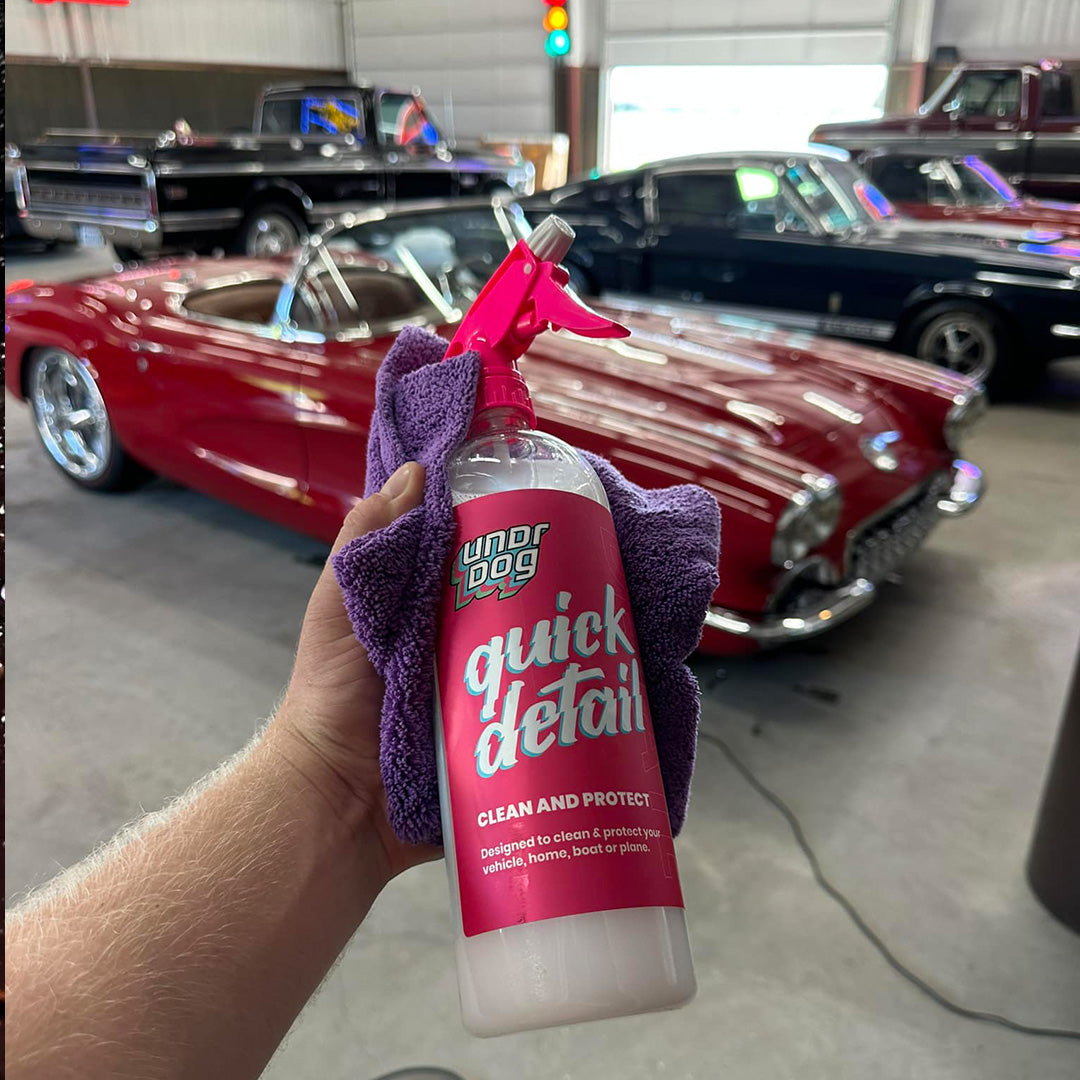 Hand holding an Undrdog Quick Detail bottle and purple towel in front of a red convertible