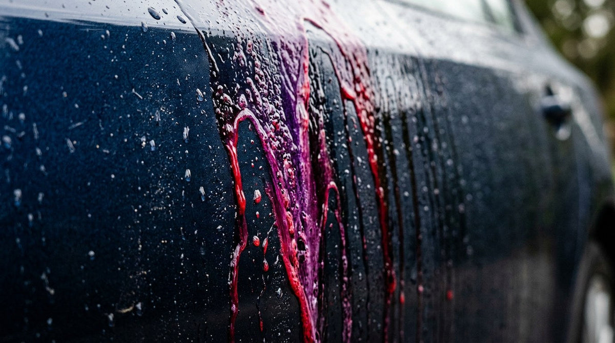 Purple iron remover streaks bleeding down dark car paint as The Purps chelates embedded iron fallout into a water-soluble complex