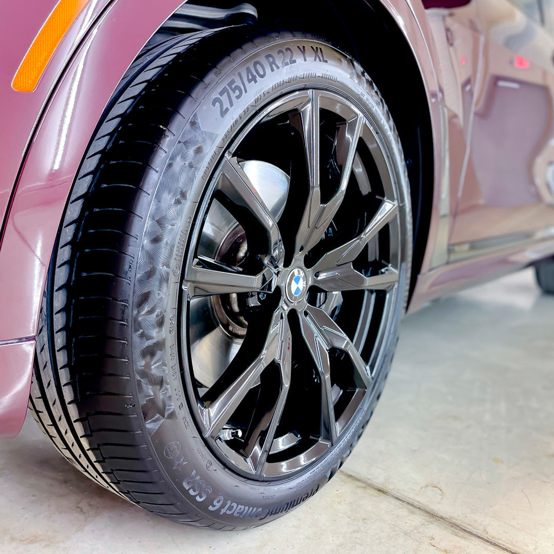 Close view of a dark multi-spoke wheel and tire on a burgundy vehicle