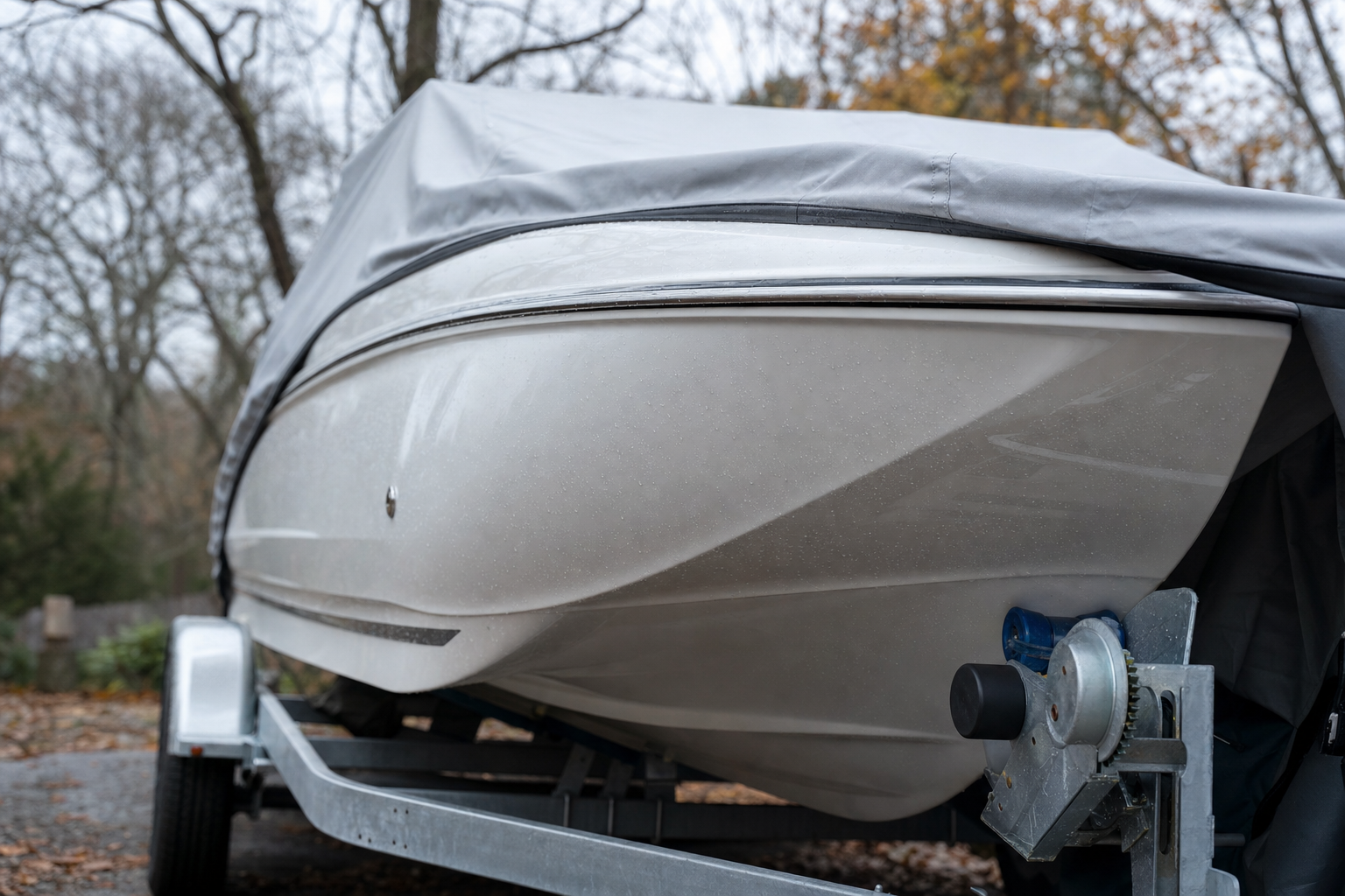 Glossy white fiberglass boat on a trailer being covered for winter storage