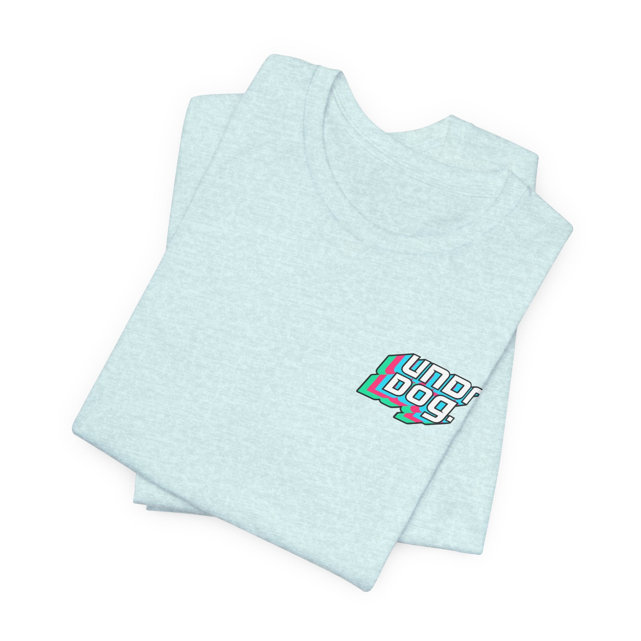 A folded light blue Unisex Jersey Short Sleeve Tee by Printify, made from soft Airlume combed cotton, showcases a small "underdog" graphic in bold, colorful text on the upper left chest. The design features fresh white, pink, and teal tones. This is a classic you’ll reach for over and over.