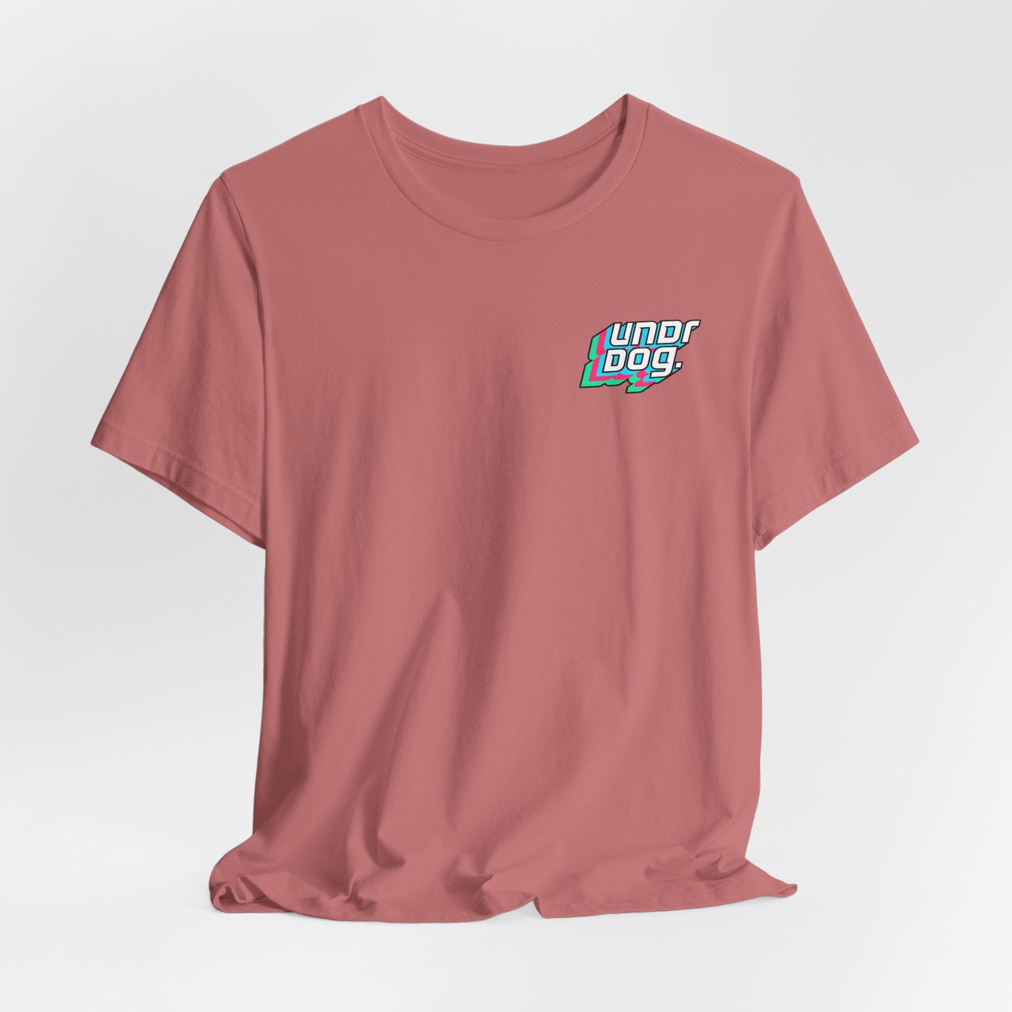 A plain mauve Printify Unisex Jersey Short Sleeve Tee, featuring a small, colorful "Underdog" graphic on the left chest. Crafted from soft Airlume combed cotton, the shirt is displayed laid flat against a white background.
