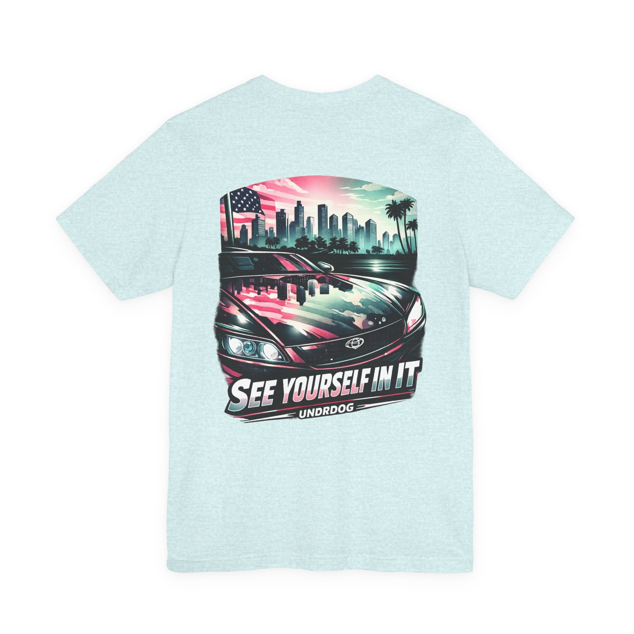 The See Yourself In It Retro Sportscar Tee by Printify features a light blue vintage car with a city skyline, palm trees, and an American flag. Below the graphic are the words "See Yourself In It" and "UNDRDOG.