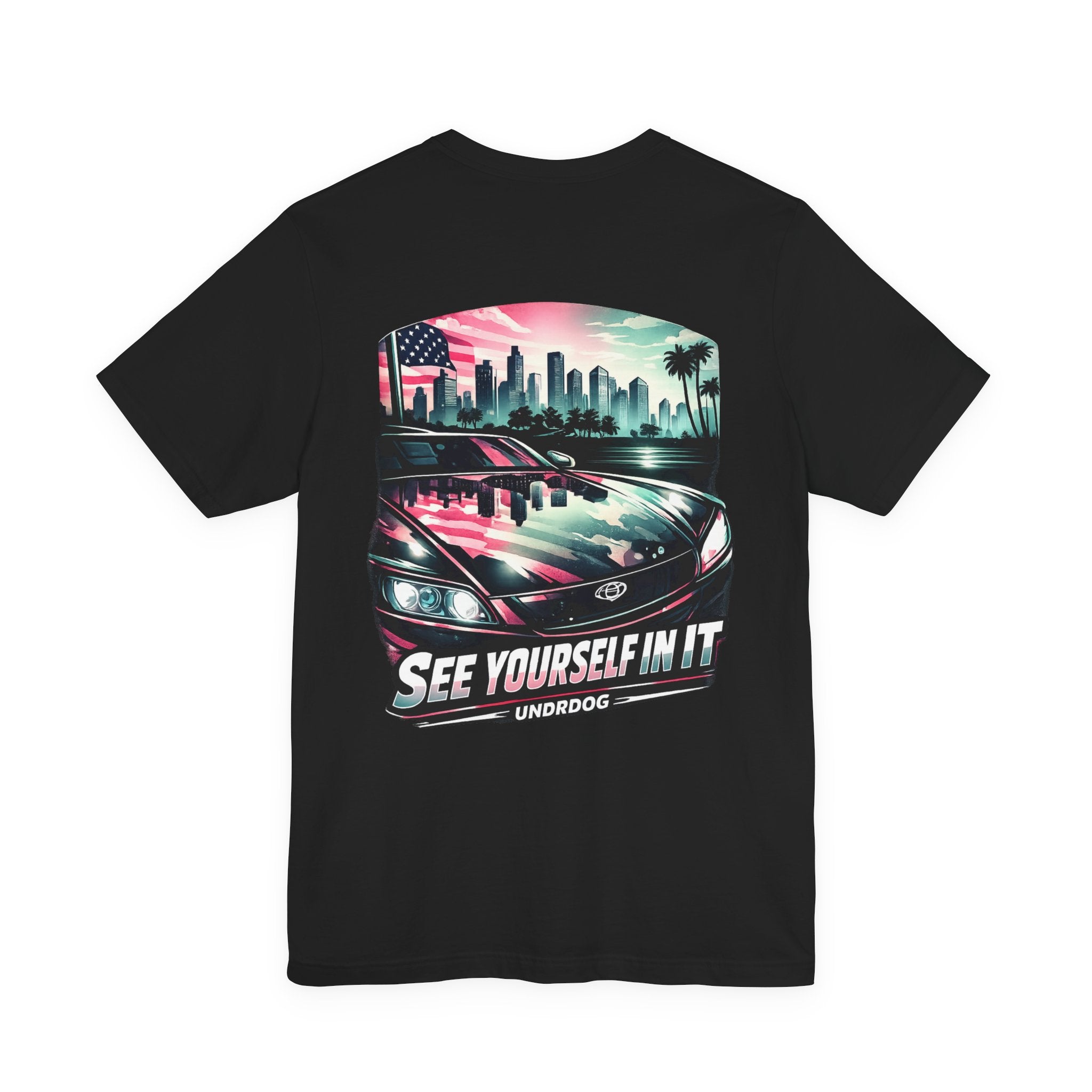 The See Yourself In It Retro Sportscar Tee by Printify features a black shirt with vintage car artwork, city skyline reflection, an American flag, palm trees, and the text “SEE YOURSELF IN IT” and “UNRDOG” below the image.